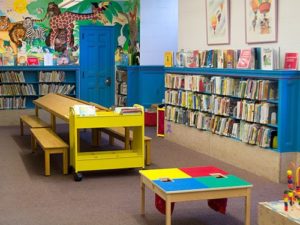 A library set up for children with low level cup boards bright colours and low level desks to sit and read